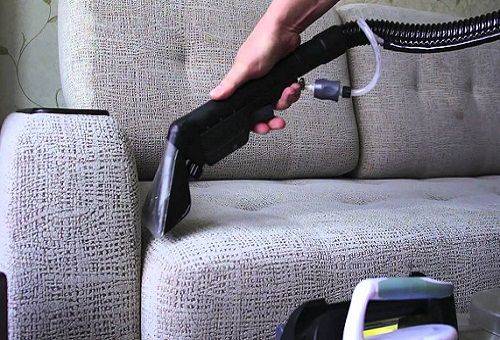 dusting the sofa with a vacuum cleaner
