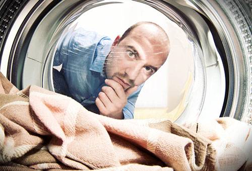 Um homem assiste a lavagem em uma máquina de lavar