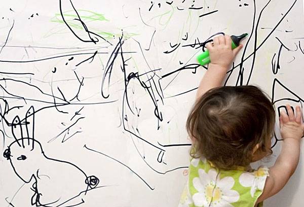 Criança desenha em uma parede branca