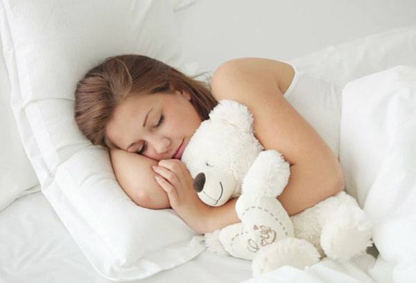 Girl sleeps in an embrace with a teddy bear.
