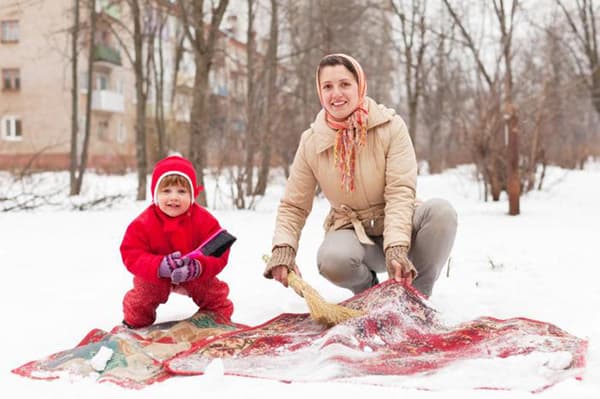 Mujer con un niño está limpiando una alfombra en la nieve.