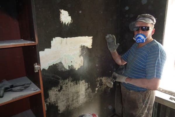 Un hombre limpia el hollín de la pared después de un incendio.