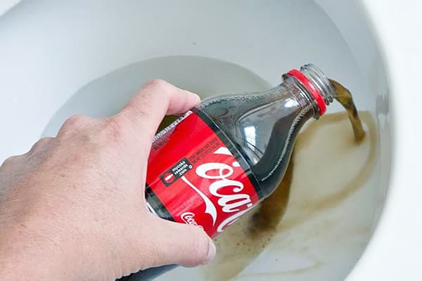 A man pours Coca-Cola into the toilet
