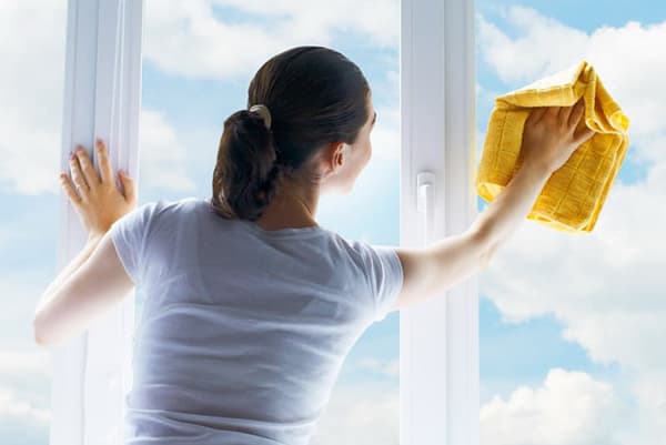 Vrouw wast een raam bij zonnig weer