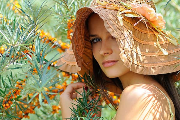 Girl in a hat near a bush of sea buckthorn