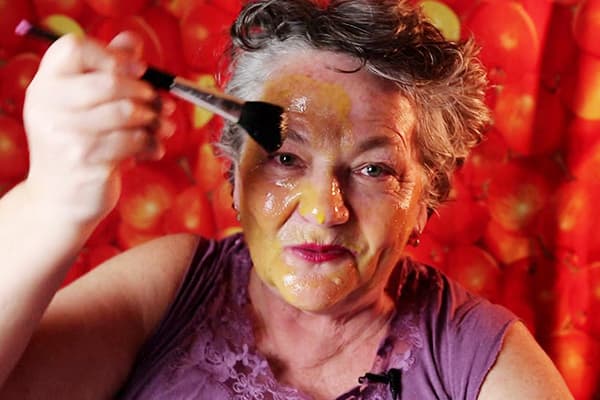 An elderly woman puts an egg mask on her face
